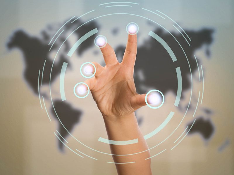 Eine Hand mit gespreizten Fingern interagiert mit virtuellen Berührungspunkten vor dem Hintergrund einer unscharfen Weltkarte